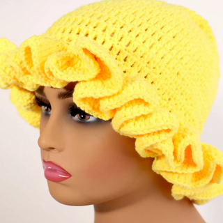 Yellow crochet hat with ruffled details on a mannequin head against a white background