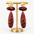 Burgundy wood and gold-tone metal drop earrings on an earring stand on a light background