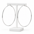 Large slim silver-tone hoop earrings hanging on a white holder