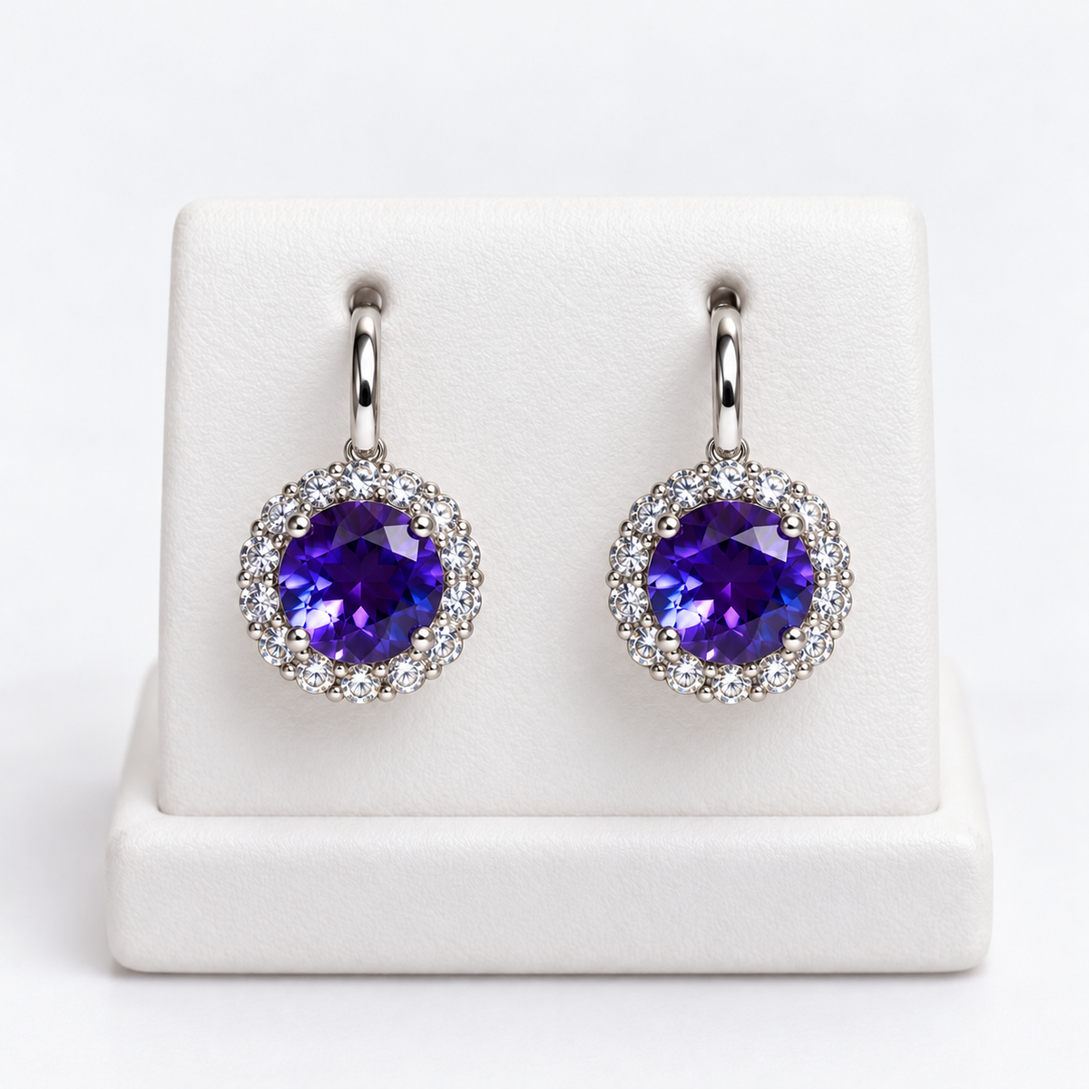 Pair of purple gemstone halo huggie earrings with clear accents and silver-colored settings on a white holder
