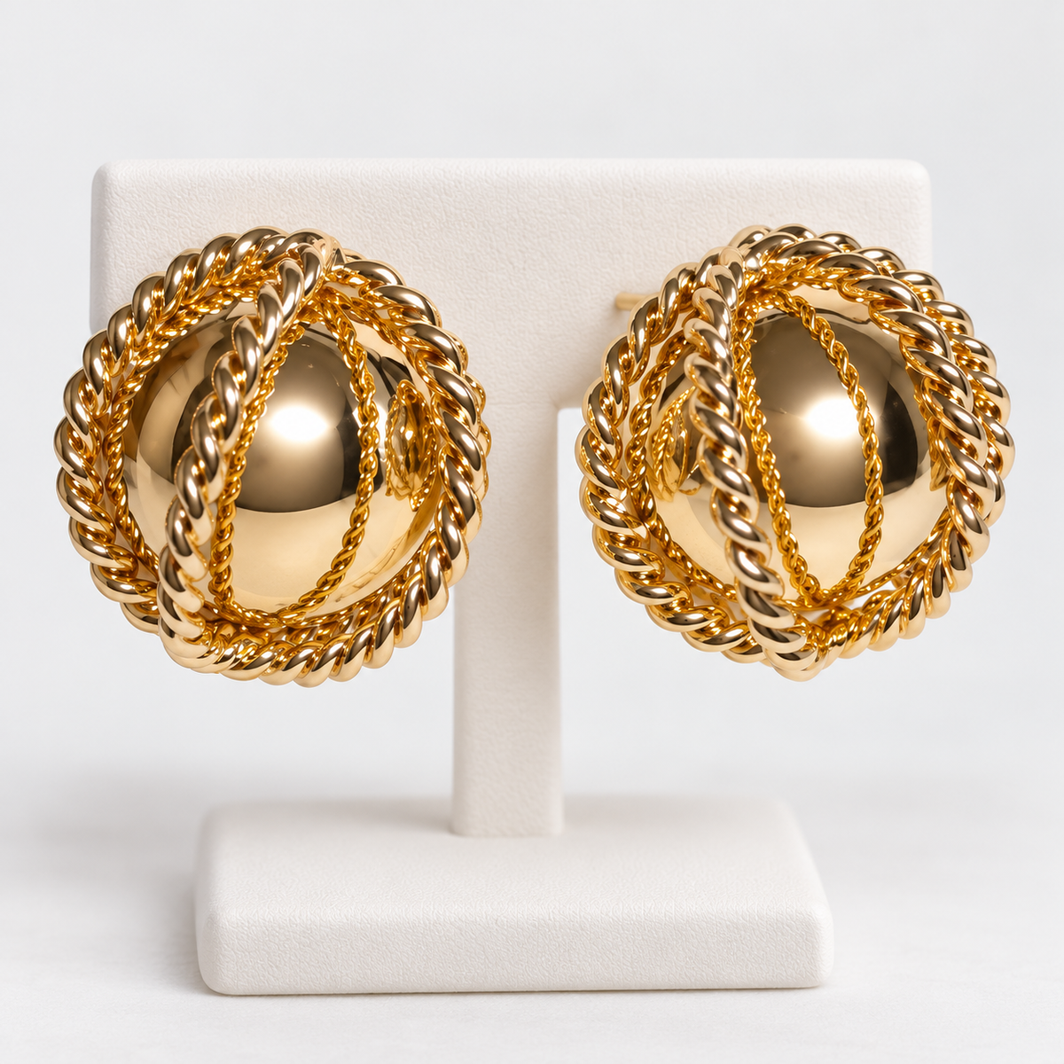 Pair of gold-dipped caged ball stud earrings with twisted rope details on a white earring holder