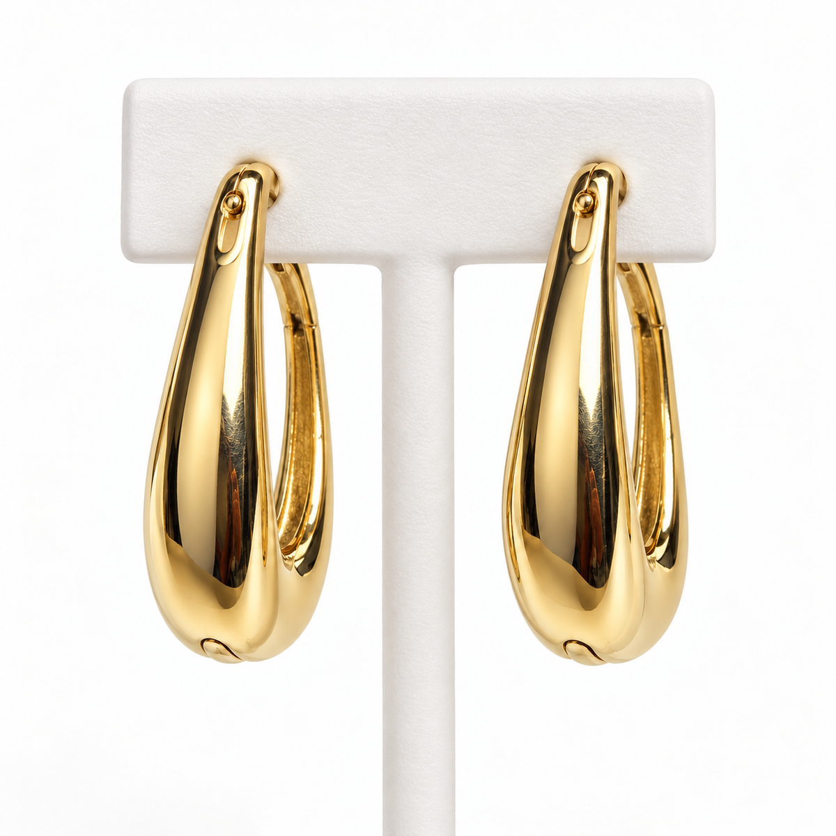 Gold-tone tapered hoop earrings hanging on a white holder
