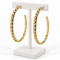 Large gold-tone faceted open hoop earrings with post backs on a white holder