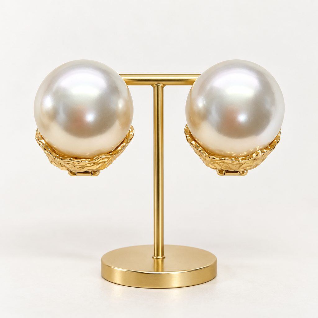 Oversized ivory pearl-look clip-on earrings in textured gold-tone settings on a holder