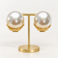 Oversized ivory pearl-look clip-on earrings in textured gold-tone settings on a holder