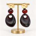 Deep dark amber dangle earrings with gold-tone tops on an earring stand