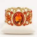 Orange crystal stretch bracelet with gold-tone floral openwork on an ivory cushion