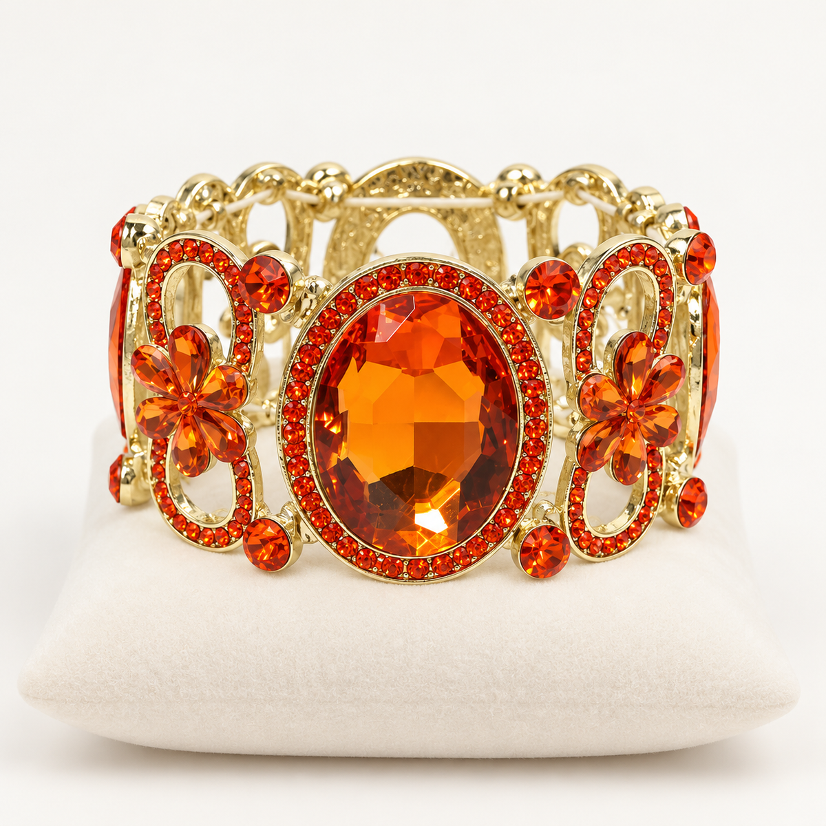 Orange crystal stretch bracelet with gold-tone floral openwork on an ivory cushion