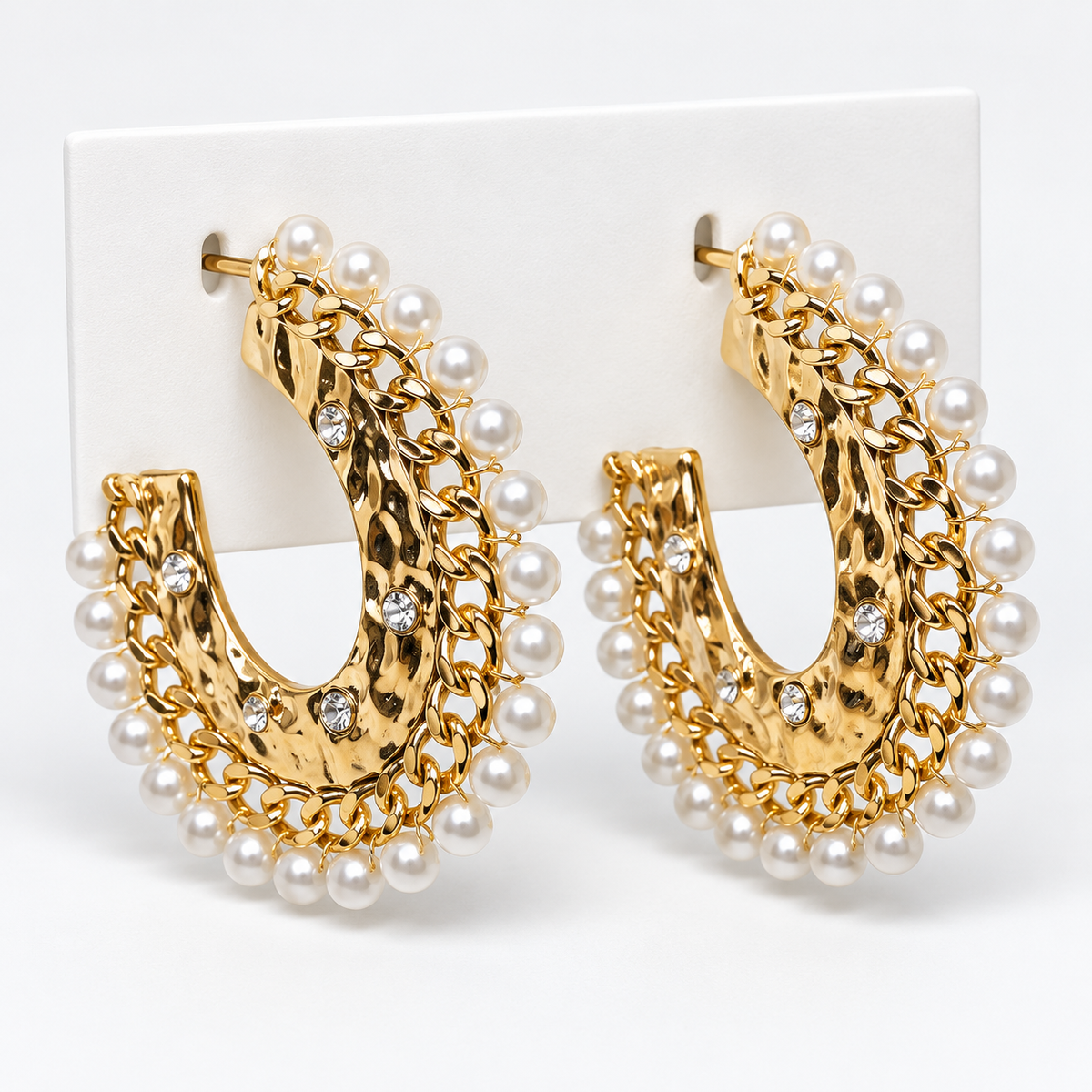 Gold-tone hammered open hoop earrings with white pearl-look trim and clear stone accents on a white holder
