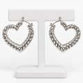 Silver-tone ribbed heart-shaped hoop earrings hanging on a white holder