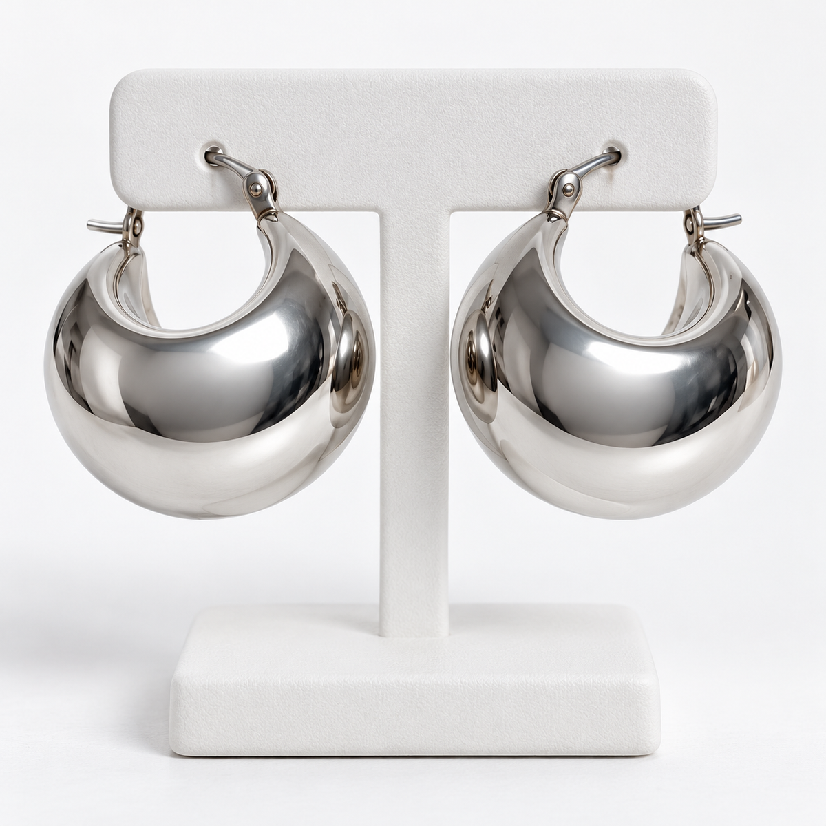 Pair of polished silver stainless steel chunky crescent hoop earrings on a white holder