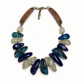 Blue hand-tied wood and chunky resin necklace laid flat in a square frame